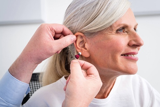 Ältere Frau bekommt ein modernes Hörgerät eingesetzt, Hörakustik und Hörhilfeberatung.